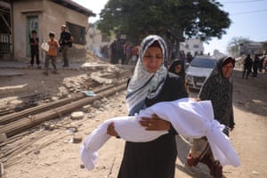 A woman carries the body of a child wrapped in a white sheet