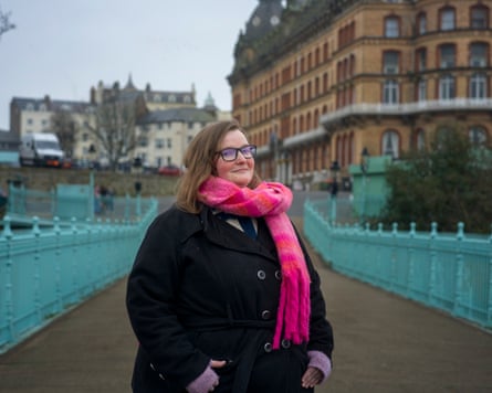 A young woman in a pink scarf standing on an iron footbridge painted sky blue