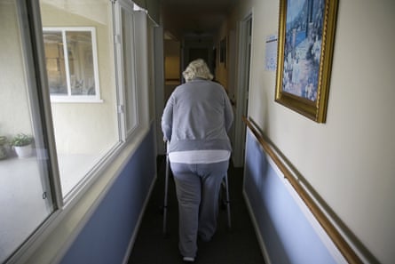 An elderly woman walks down a hallway.