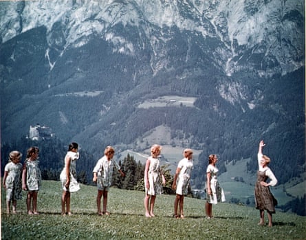 Julie Andrews standing with her arm in the air in front of a row of children in the alps