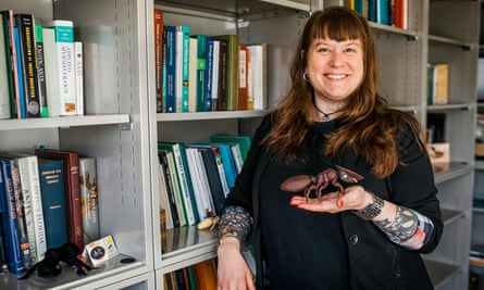 Corrie Moreau stands in front of book shelves with a model of a giant ant on the palm of her hand.