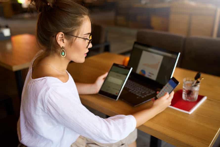 Mixed race woman in glasses working with multiple electronic internet devices. Freelancer businesswoman has tablet and cellphone in hands and laptop on table with charts on screen. Multitasking themePosed by model Mixed race woman in glasses working with multiple electronic internet devices. Freelancer businesswoman has tablet and smartphone in hands and laptop on table with charts on screen. Multitasking and telecommuting theme.
