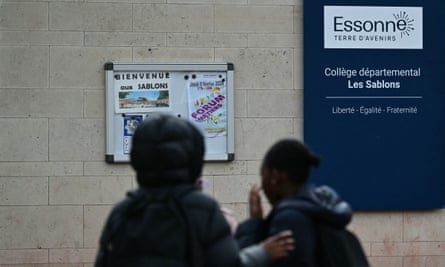Two young people stand at the entrance to a school in France reading a noticeboard