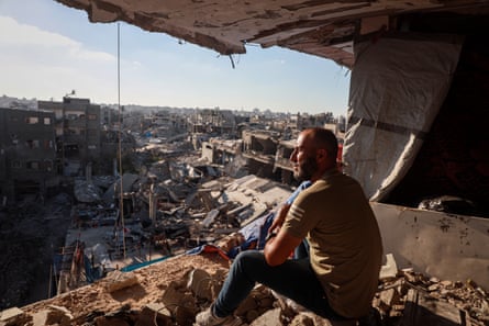 A man sits in the rubble of a building looking out at other damaged buildings