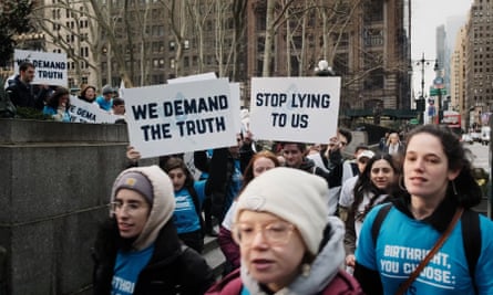 people hold signs that say ‘we demand the truth’ and ‘stop lying to us’