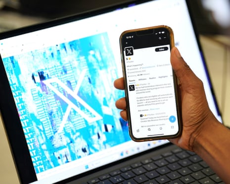 A person holds a smartphone aloft in front of a laptop screen, with both screens displaying the X app or website.