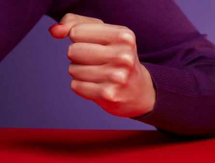 Woman’s clenched fist , arm leaning on red table top