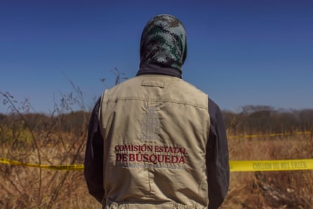 a person photographed from behind looks at scrub of land behind crime scene tape