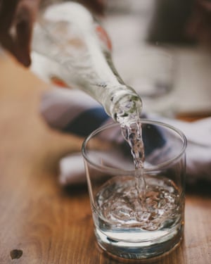 Woman Pouring Water From Glass Bottle Into Drinking Glass