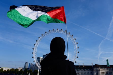 A person holds a Palestinian flag with their back to the camera with the London Eye in the background
