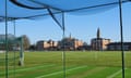 View looking outwards from cricket nets on to a playing field, with the college's terracotta renaissance-style buildings in the distance.