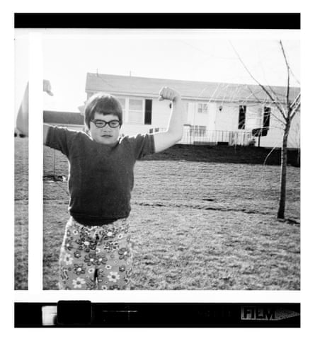 Opie as a child striking a strongman pose with a park and houses in the background, black and white image.