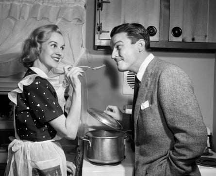 in black and white, 50s-style photo, a woman cooks and holds out some food for a man to taste