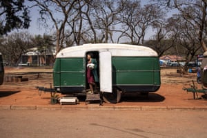 Daphne Siwardi in profile holding a white bouquet in the doorway of her green caravan parked in the red sand outside Harare magistrates court