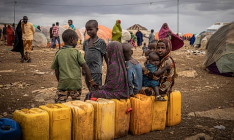 Niños sentados en botellas de agua esperando a ser llenadas entre tiendas de campaña en un campamento de desplazados para personas afectadas por la sequía en Baidoa, Somalia.