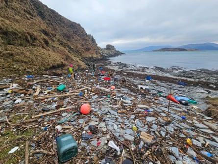 A small bay with two people and dogs standing amid lots of plastic rubbish, such as traffic cones, jerrycans and floats