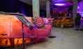 Two totally burnt out cars, one upside down, illuminatewd with orange light, form part of an exhibit
