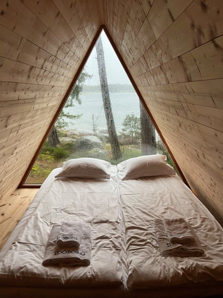 A triangular wooden cabin with a bed and view of the sea and forest