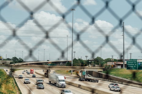 Cars and trucks driving on a highway seen through a chainlink fence.