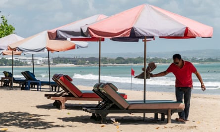 A man sets up sea-side loungers at a beach in Kuta, Bali, Indonesia