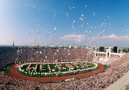 Helium balloons are released into the air from a packed stadium. 'Welcome' is spelled out on the field 