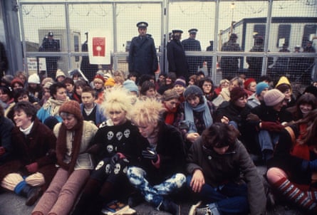 A large group of woman of various ages sit outside Greenham Common air base in a photo from 1983