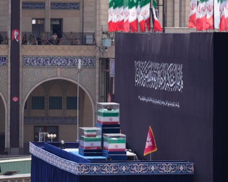 Three coffins in glass cases, draped in the Iranian flag, on a tall platform