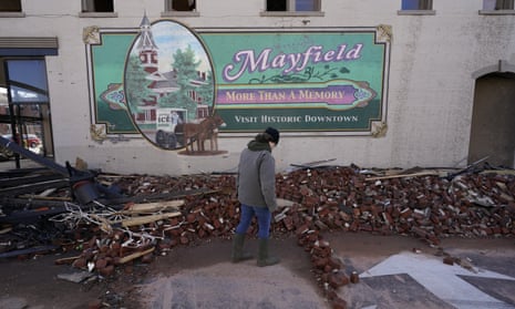 A person walks past the rubble of a building in front of a mural with the message, "Mayfield: more than a memory. Visit historic downtown."