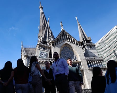 People outside a cathedral with one of three spires leaning at an angle