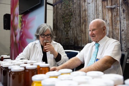 Two people stand behind a table full of honey jars, one person is lifting a jar to their nose