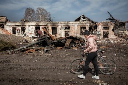 A resident of Trostianets pushes her bicycle past destroyed Russian military equipment.