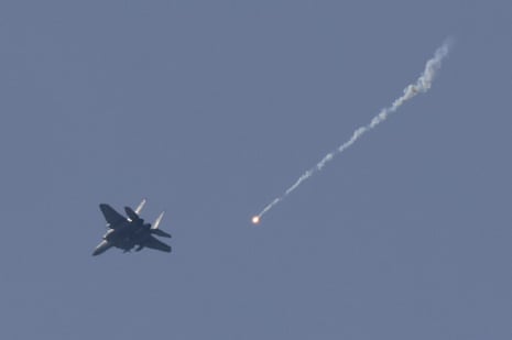 Истребитель летит на фоне серо-голубого неба, за ним горит ракета.