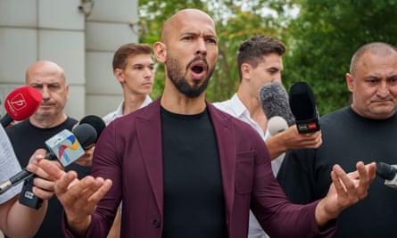 Andrew Tate with his arms outstretched. He is surrounded by people holding microphones.