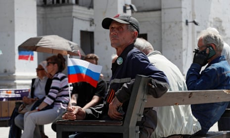 A man holds a Russian flag as he sits in front of a destroyed theatre building in Mariupol