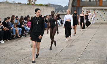 Models walk along a paved area of Cité Radieuse as people sit watching at the side