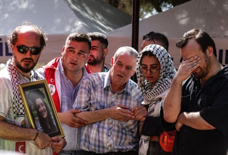 Closeup of five people in a row, with an older man in the middle being held up by people on both sides of him.