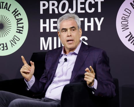 Jonathan Haidt makes a pointing gesture with both hands as he speaks on stage, with a Project Health Minds banner behind him
