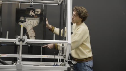 Man in a cream jumper transports the portrait using some sort of metal machine