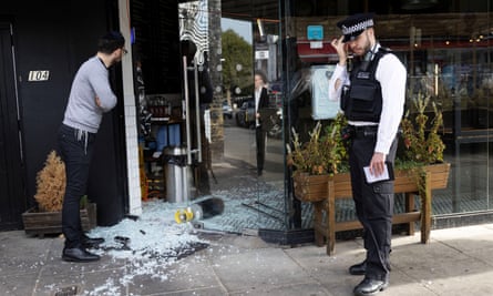 A man and a police officer stand next to a vandalised Kosher restaurant