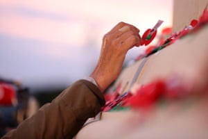 A hand placing a paper poppy on the cenotaph at Auckland Museum.