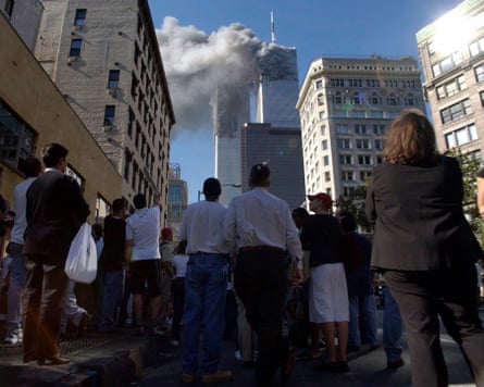 Pedestrians stand in the street and watch the smoke billowing out of the World Trade Center