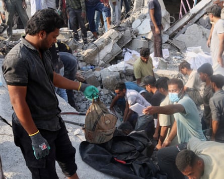 A man holds a children's backpack as rescue workers and residents search through the rubble