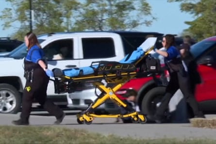 Group of emergency responders wheel stretcher through parking lot towards soccer field outside