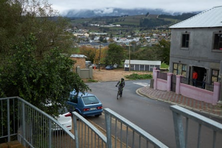 A man cycles through a residential area of houses and parked cars
