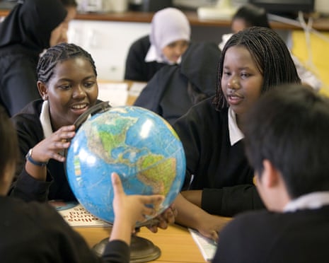 Students in school uniforms gather around a globe on a desk, smiling and pointing