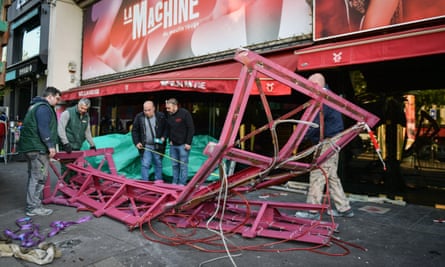 Workers tie ropes to the twisted, damaged blades as they prepare to take them away from outside the Moulin Rouge 