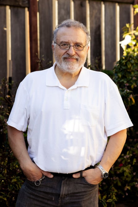 A man in a white shirt and black jeans standing for a photograph with his hands in his pockets.