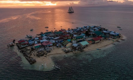 The Greenpeace ship, Rainbow Warrior, sails behind Bilangbilangan, a tiny and very low-lying island with some buildings crumbling into the sea