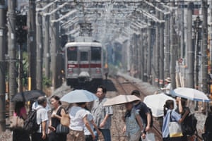 People with umbrella cross a railway track as a train emerges from the heat haze in the background