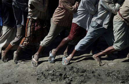 The legs and feet of labourers working in tandem to move an object on the beach.